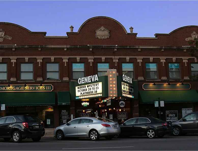 A theater with a brightly lit marquee in downtown Geneva at night 